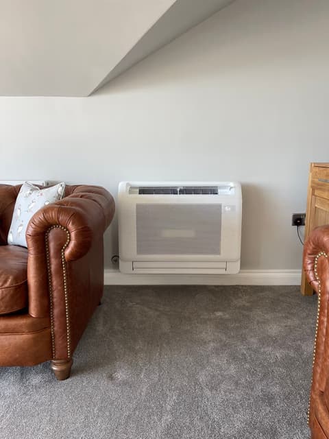 Floor-mounted console air conditioner beside a leather sofa